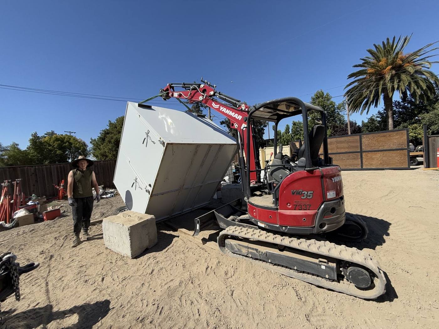 Excavator lifting and setting a large steel enclosure